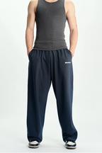 A man modeling a dark gray ribbed tank top and navy blue sweatpants against a plain white studio background.