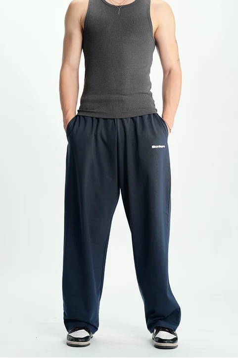 A man modeling a dark gray ribbed tank top and navy blue sweatpants against a plain white studio background.