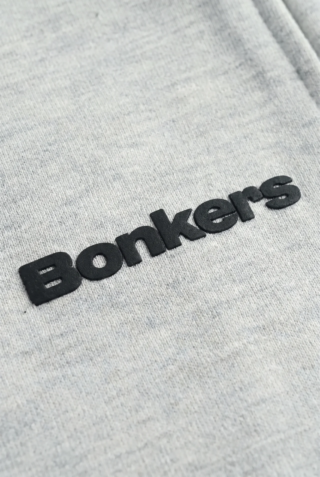 Close-up of a light heather gray fabric with a black 3D embroidered 'Bonkers' logo.