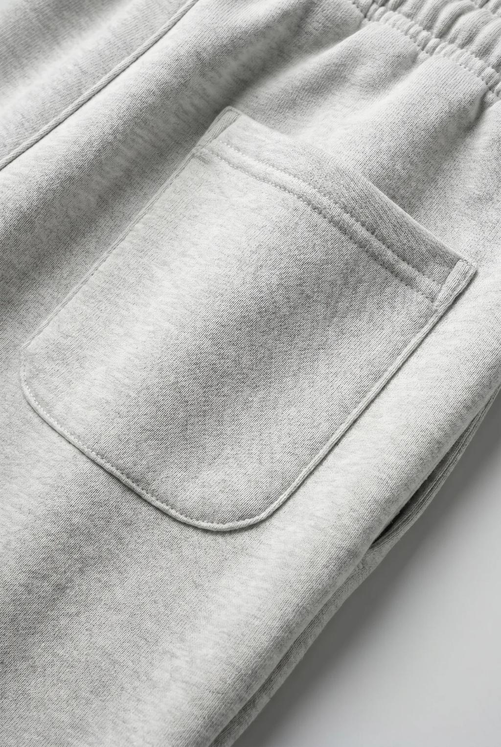 Close-up of light heather gray sweatpants showing an elastic waistband and a front patch pocket.