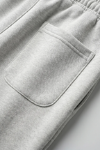 Close-up of light heather gray sweatpants showing an elastic waistband and a front patch pocket.