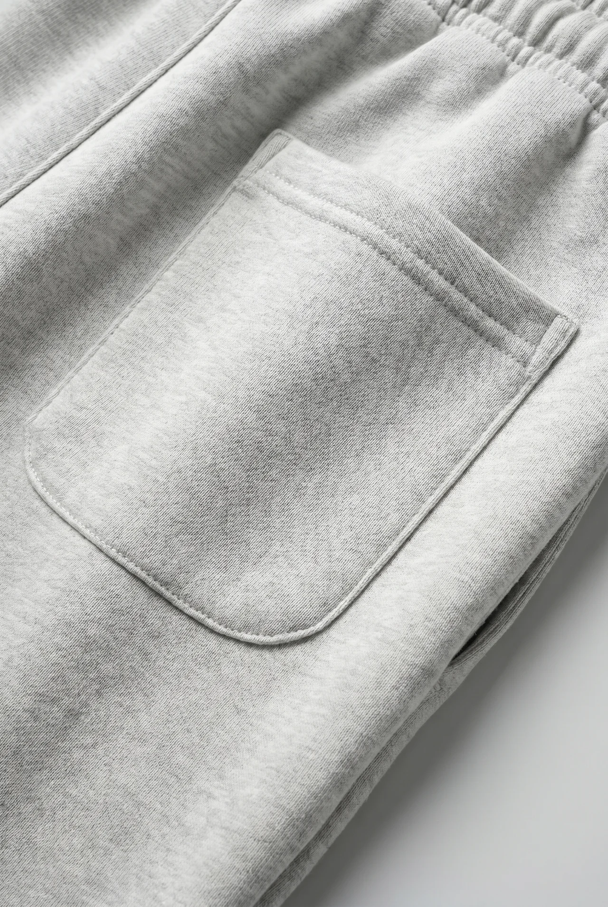Close-up of light heather gray sweatpants showing an elastic waistband and a front patch pocket.